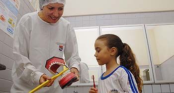 Dentista orientando escovação à aluna Livia Coelho
