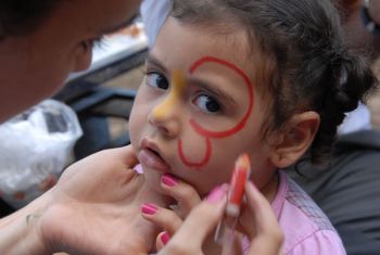 Profissional segurando rosto de criança por volta de três anos tendo o rosto pintado