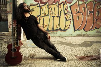 Andre Prando, com violão, em frente a um grafiti