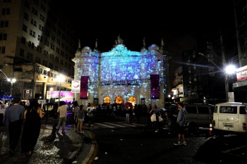 Teatro iluminado com projeção, pessoas na rua