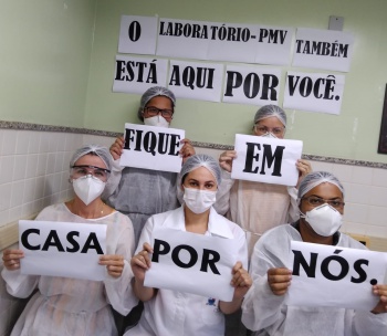 Equipe do laboratório segura cartazes onde pede para a população ficar em casa