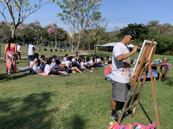 Artista "Fel Vint2" produz pintura em tela enquanto estudantes participam de piquenique poético